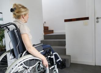 A lady in a wheelchair stares at the bottom of some stairs